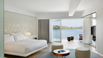 A modern hotel room with a large bed, a balcony with a view of the sea, and a flat-screen TV.