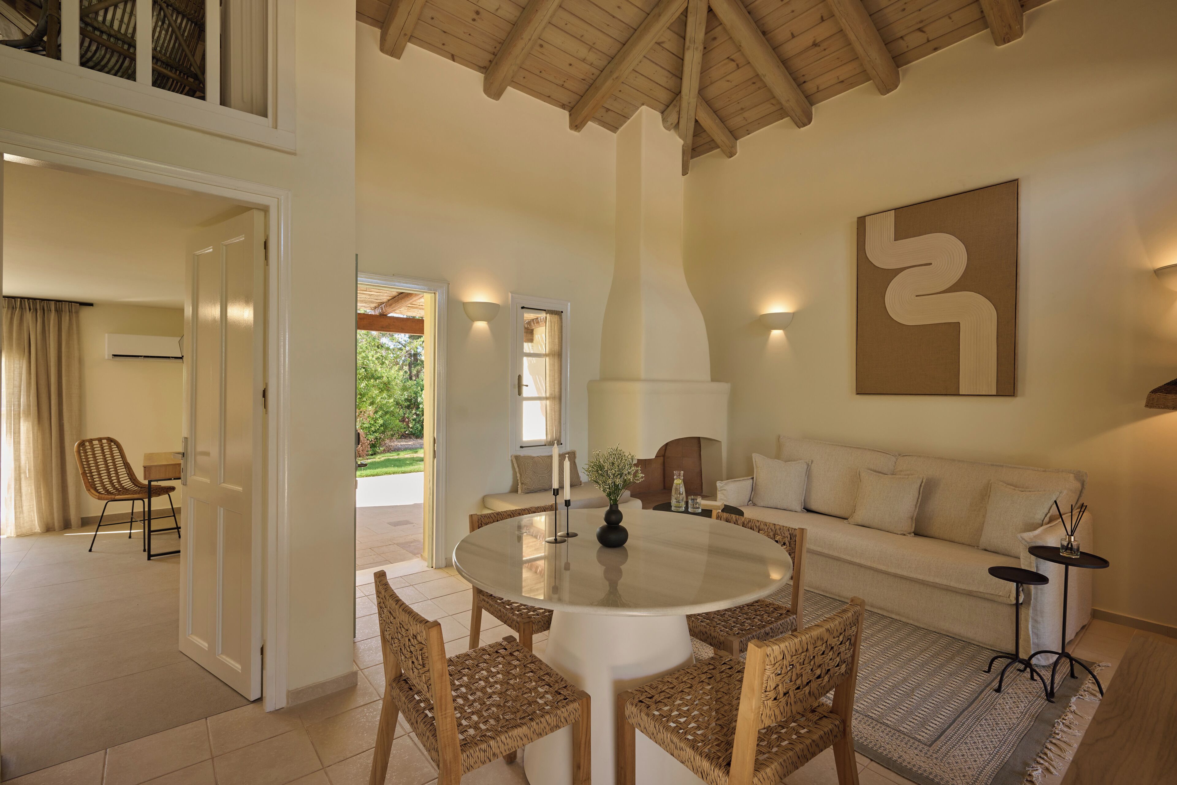 A spacious living room with a round dining table, wicker chairs, a sofa, and a large abstract painting on the wall.