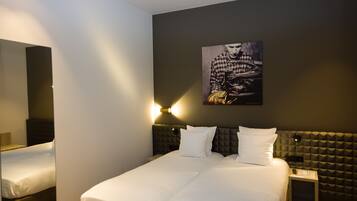 Habitació d'hotel amb un llit gran, un panell de llit amb un disseny texturat, una obra d'art penjada a la paret i una taula de nit amb una làmpada.