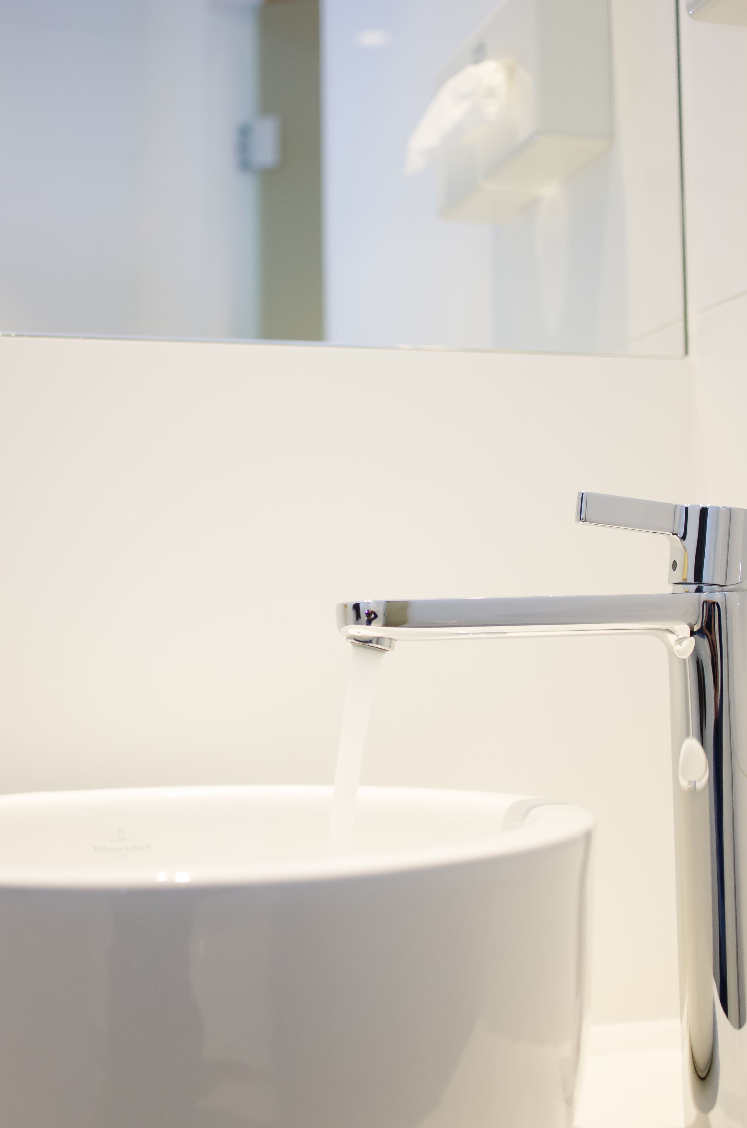 A modern bathroom with a white sink, chrome faucet, and a mirror reflecting the interior.