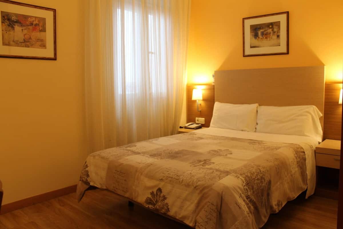 A hotel room with a bed, a nightstand, a lamp, and a window with curtains.