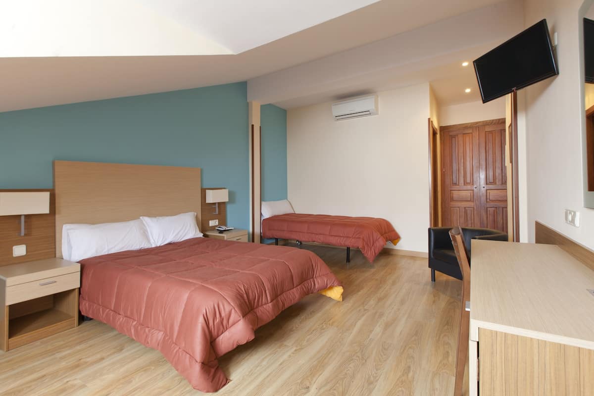 A hotel room with two beds, a desk, a chair, a TV, and an air conditioning unit.