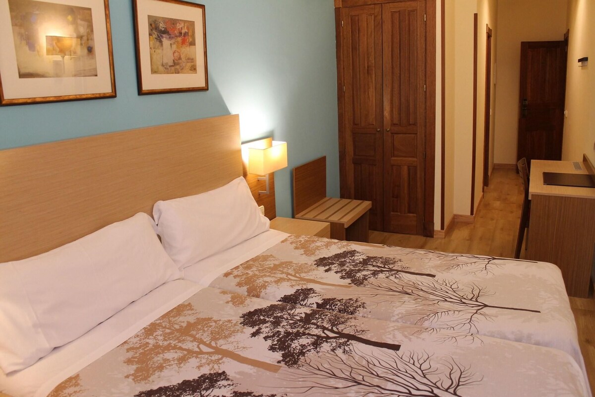 A hotel room with a bed, a nightstand, a desk, and a wardrobe.