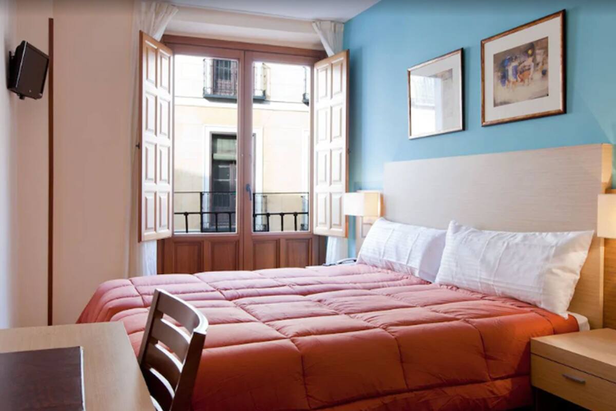 A hotel room with a bed, a nightstand, a chair, and a window with an open door.