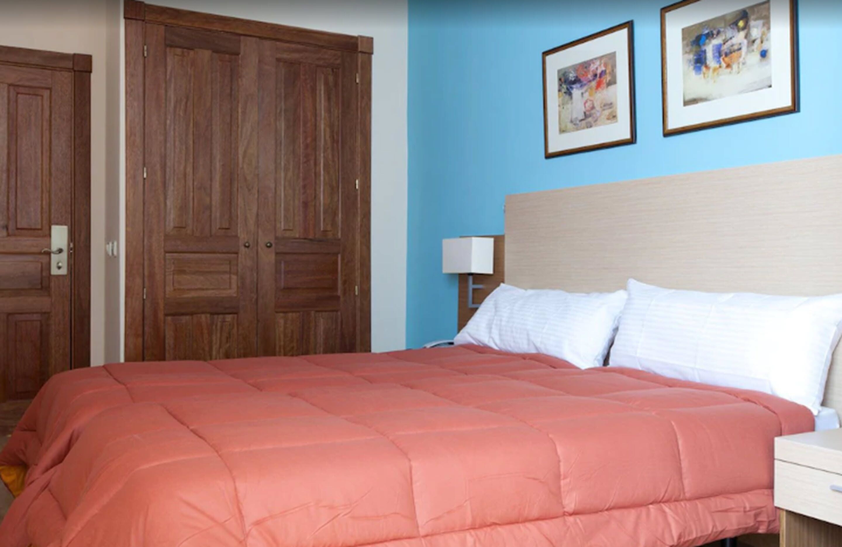 A bedroom with a large bed, wooden wardrobe, and two framed pictures on the wall.