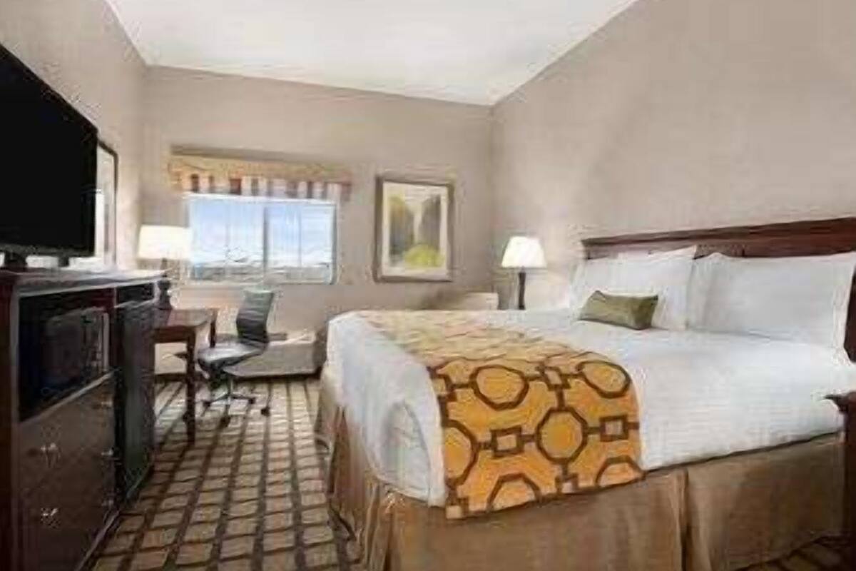 Een hotelkamer met een bed, een bureau, een stoel, een televisie en een raam met gordijnen.