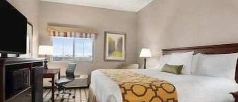 A hotel room with a bed, a desk, a chair, a television, and a window with curtains.