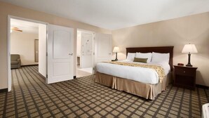 A hotel room with a large bed, two bedside lamps, a nightstand, and a patterned carpet. - Baymont by Wyndham Odessa (Odessa)