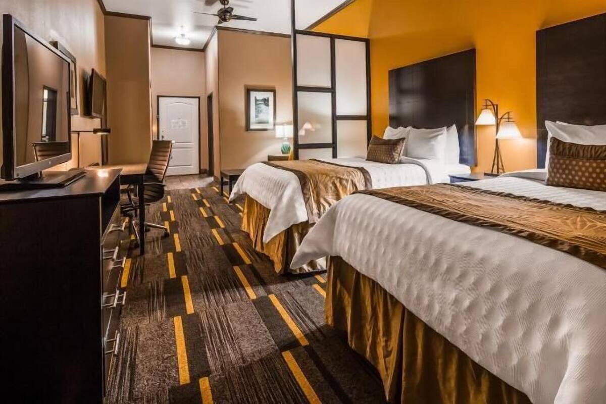 A hotel room with two beds, a desk, a TV, and a bathroom.