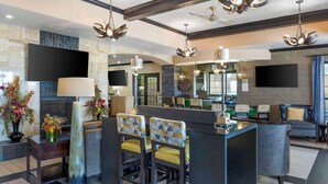 Un hall d’hôtel moderne doté d’un bar, de coins salon et d’un grand écran de télévision.