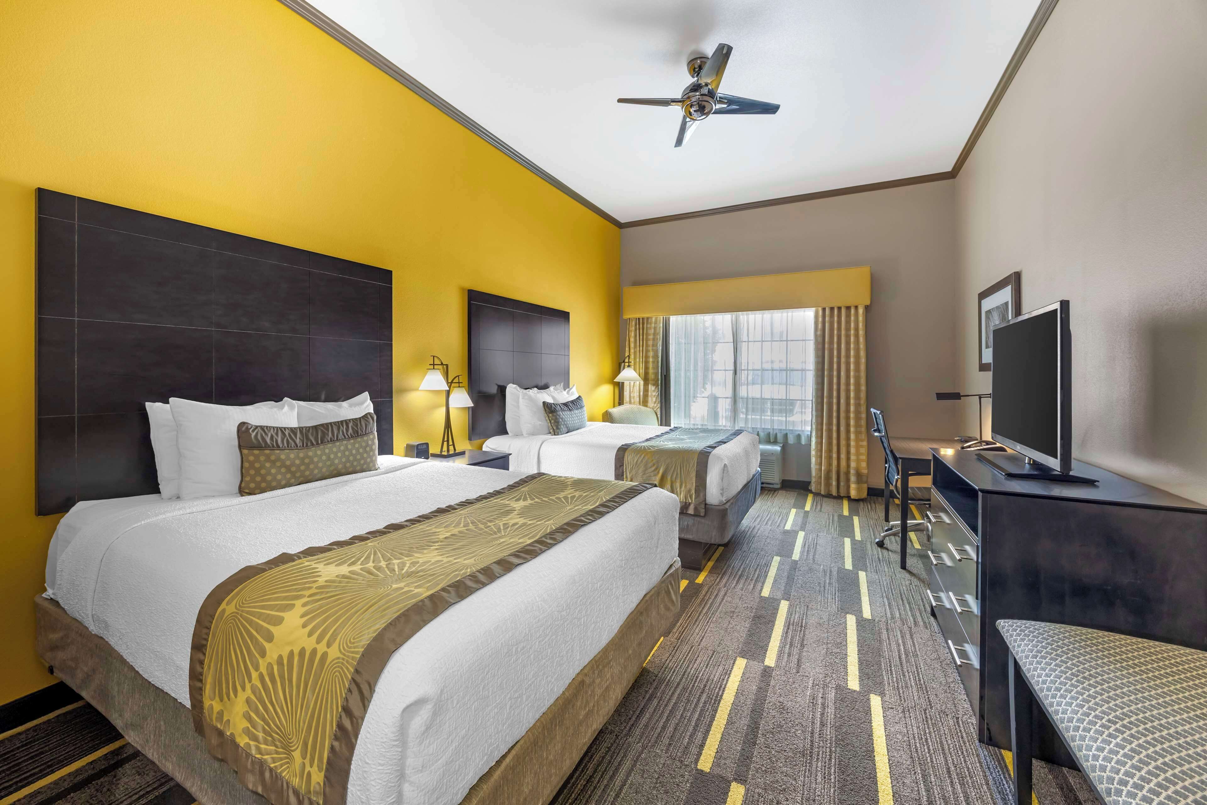 A hotel room with two beds, a desk, a television, and a ceiling fan.