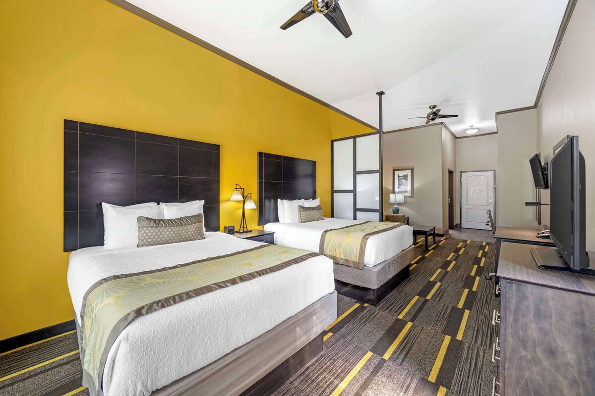 A hotel room with two beds, a ceiling fan, a TV, and a desk.