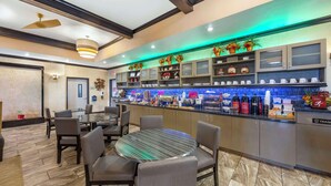 Un hall d’hôtel moderne avec une table de salle à manger ronde, des sièges confortables, un bar avec des étagères remplies de bouteilles et des plantes décoratives.
