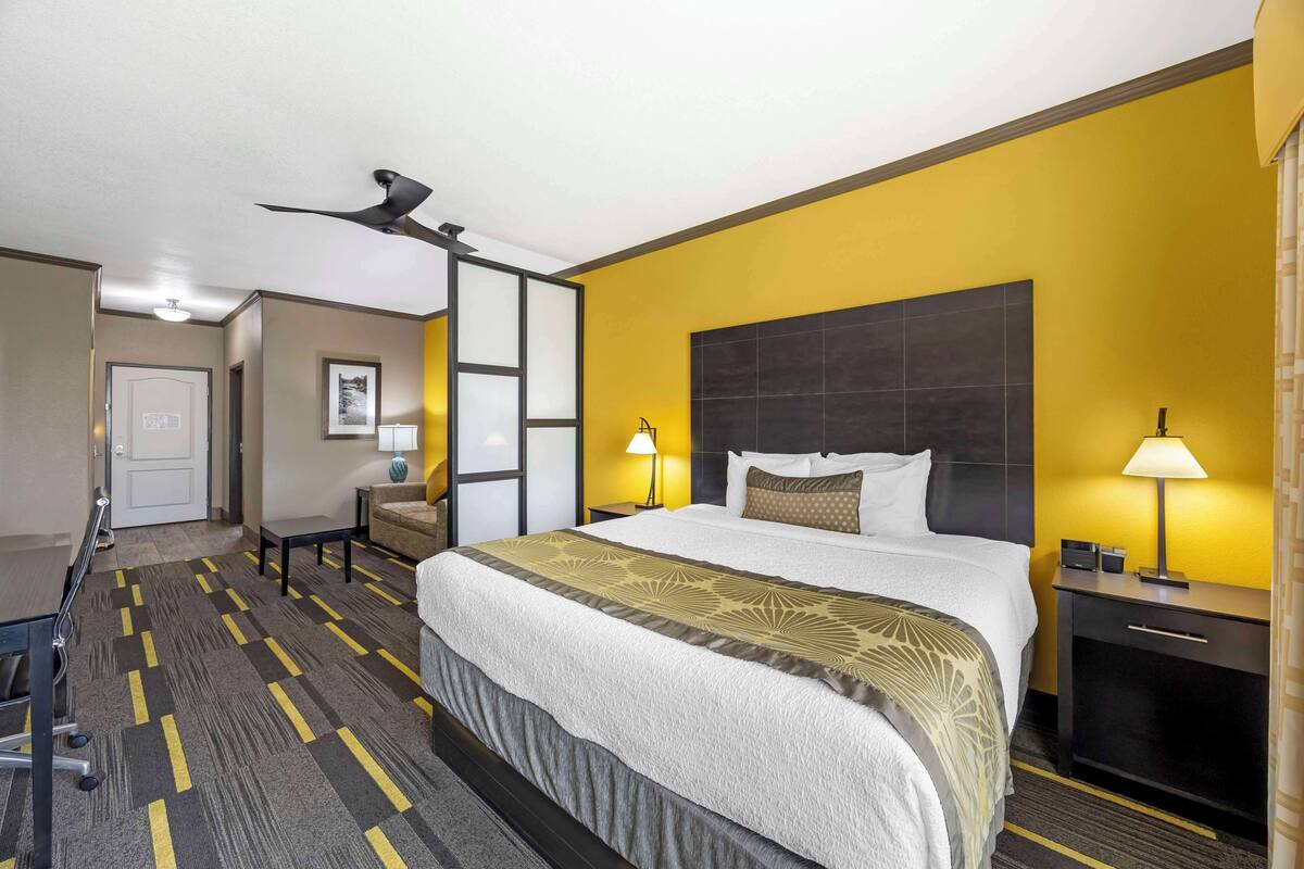 A hotel room with a large bed, two bedside lamps, a ceiling fan, and a desk with a chair.
