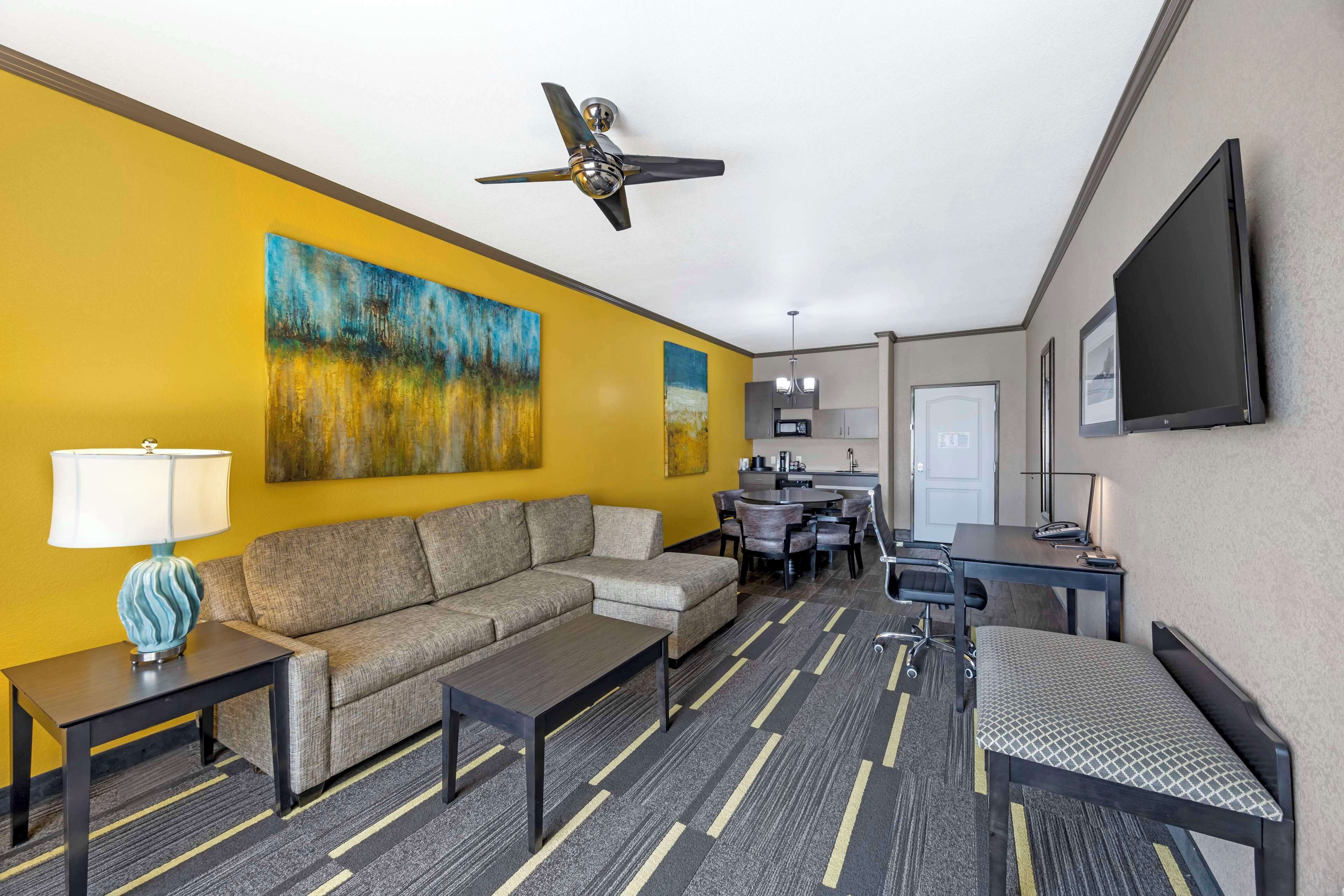 A hotel room with a sofa, a coffee table, a desk, a chair, a TV, and artwork on the wall.