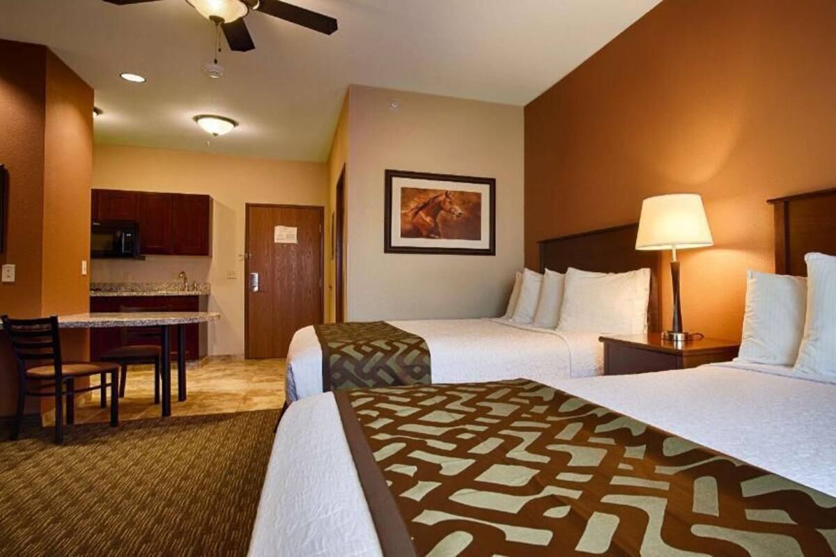 A hotel room with two beds, a desk, a chair, a lamp, and a ceiling fan.