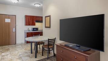 A compact kitchen with a granite countertop, wooden cabinets, a microwave, and a flat-screen TV on a wooden stand.