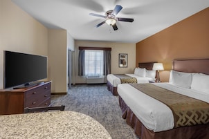 Habitación de hotel con cama, televisor, ventilador de techo y ventana con cortinas.