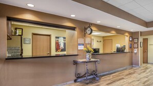 A reception area with a wooden reception desk, a clock, framed certificates, and a vase with flowers. - Best Western North Edge Inn (Dodge City)