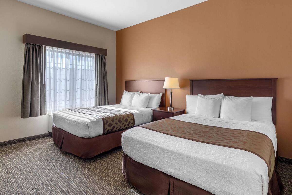 A hotel room with two beds, a nightstand with a lamp, and a window with curtains.
