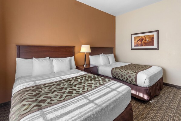 A hotel room with two beds, a nightstand with a lamp, and a framed picture on the wall.