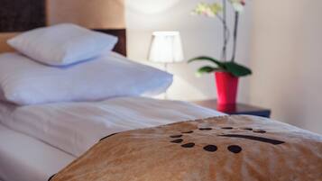 A neatly made bed with white linens, a bedside lamp, and a red vase with flowers.