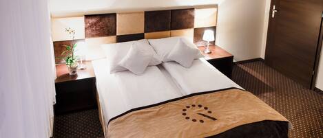 A hotel room with a neatly made bed, a nightstand with a lamp, and two framed pictures on the wall.