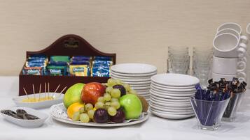 Una mesa con una bandeja de frutas, platos, vasos y una caja de bombones.