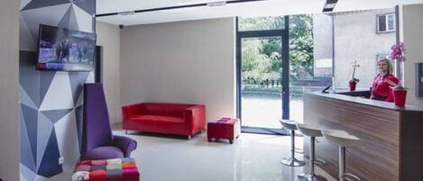 A modern hotel lobby with a red sofa, a purple armchair, and a bar area with stools.