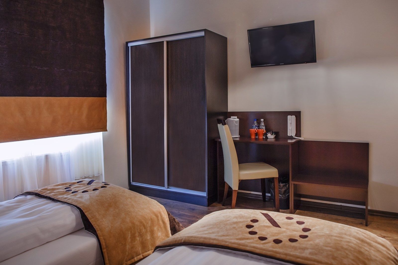 A hotel room with two beds, a desk, a chair, a TV, and a wardrobe.