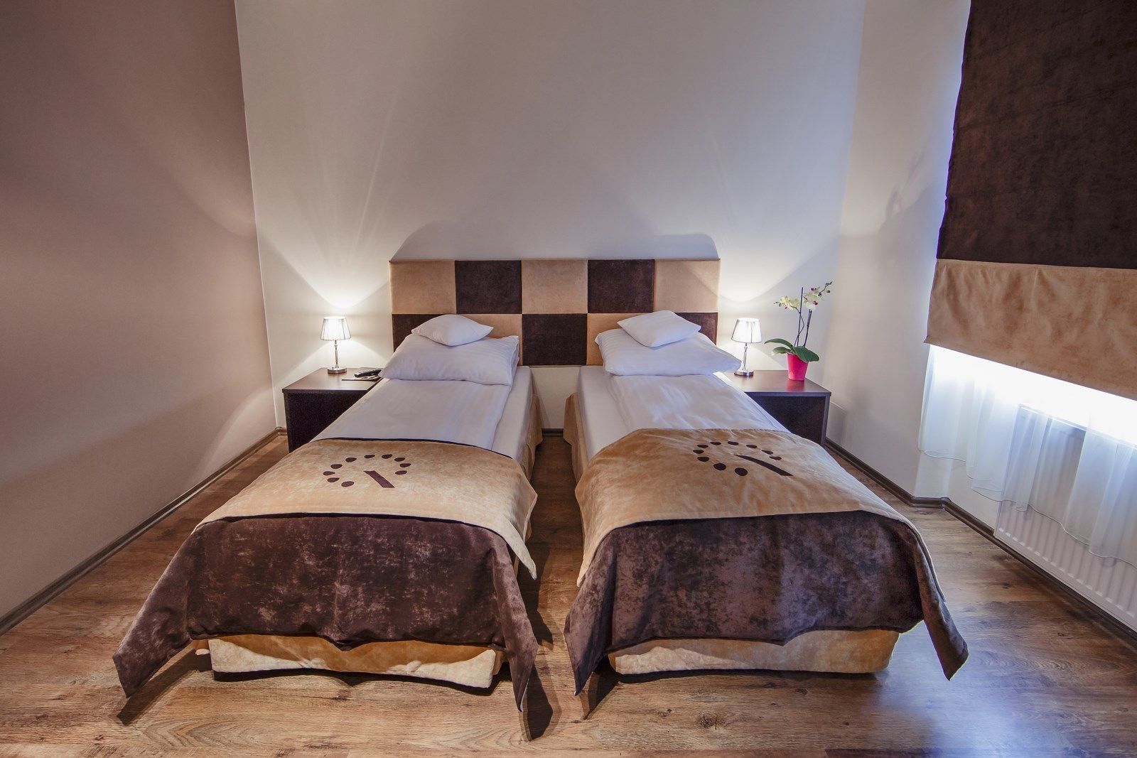 A hotel room with two beds, a checkered headboard, bedside lamps, and a potted plant.