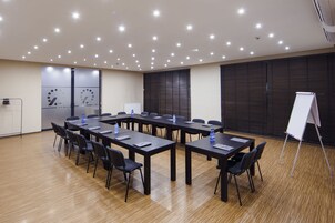 Uma sala de conferência com uma mesa comprida, cadeiras, um quadro branco e um bebedouro.