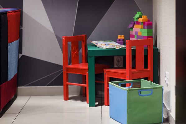 A room with a green table, two red chairs, and a colorful play structure.