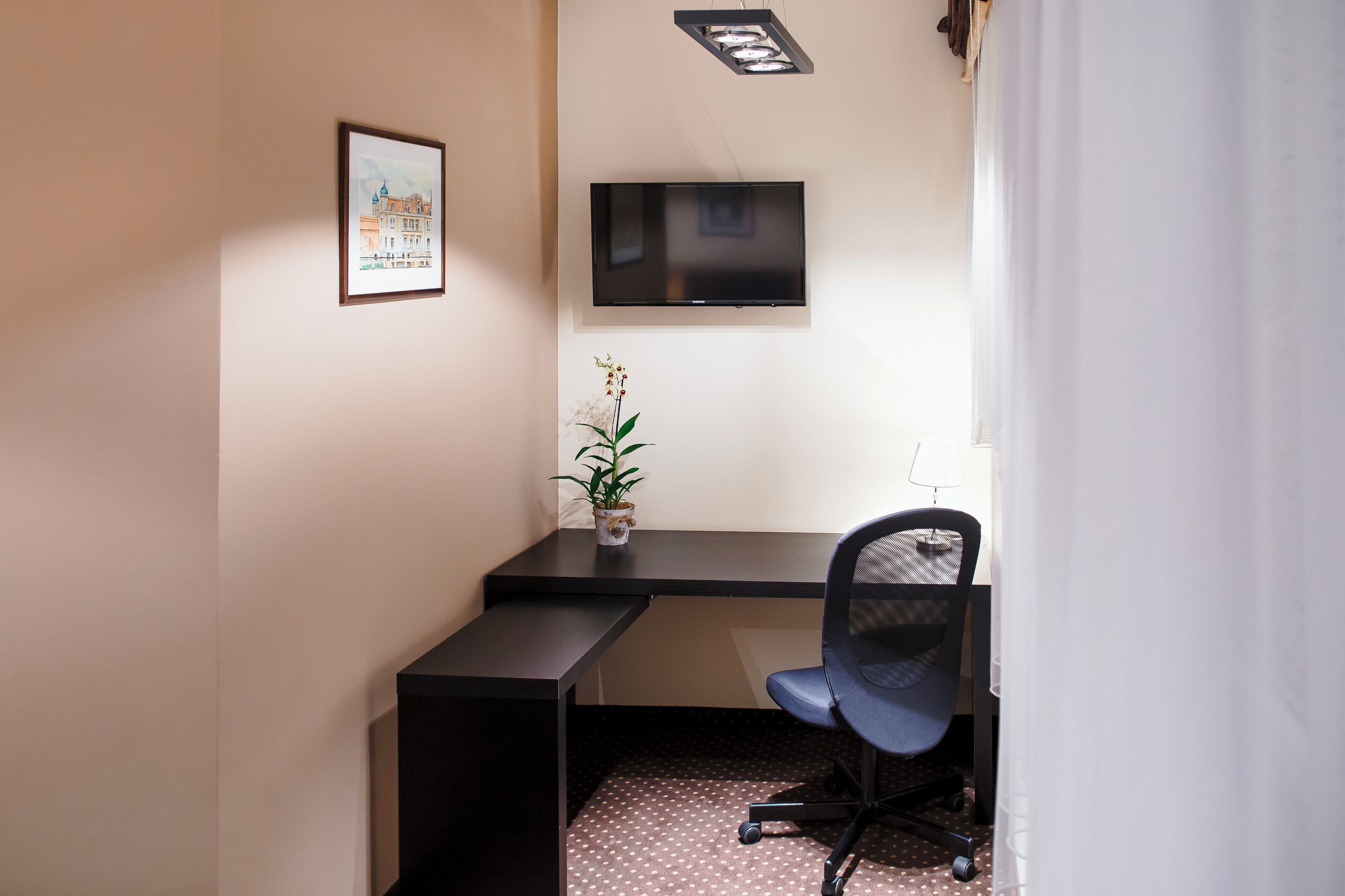 Een kleine kantoorruimte met een bureau, stoel en een wandgemonteerde flatscreen televisie.