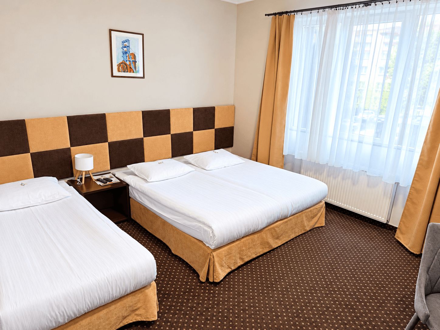 Habitación de hotel con dos camas, una mesita de noche, una lámpara, un cuadro en la pared y una ventana con cortinas.