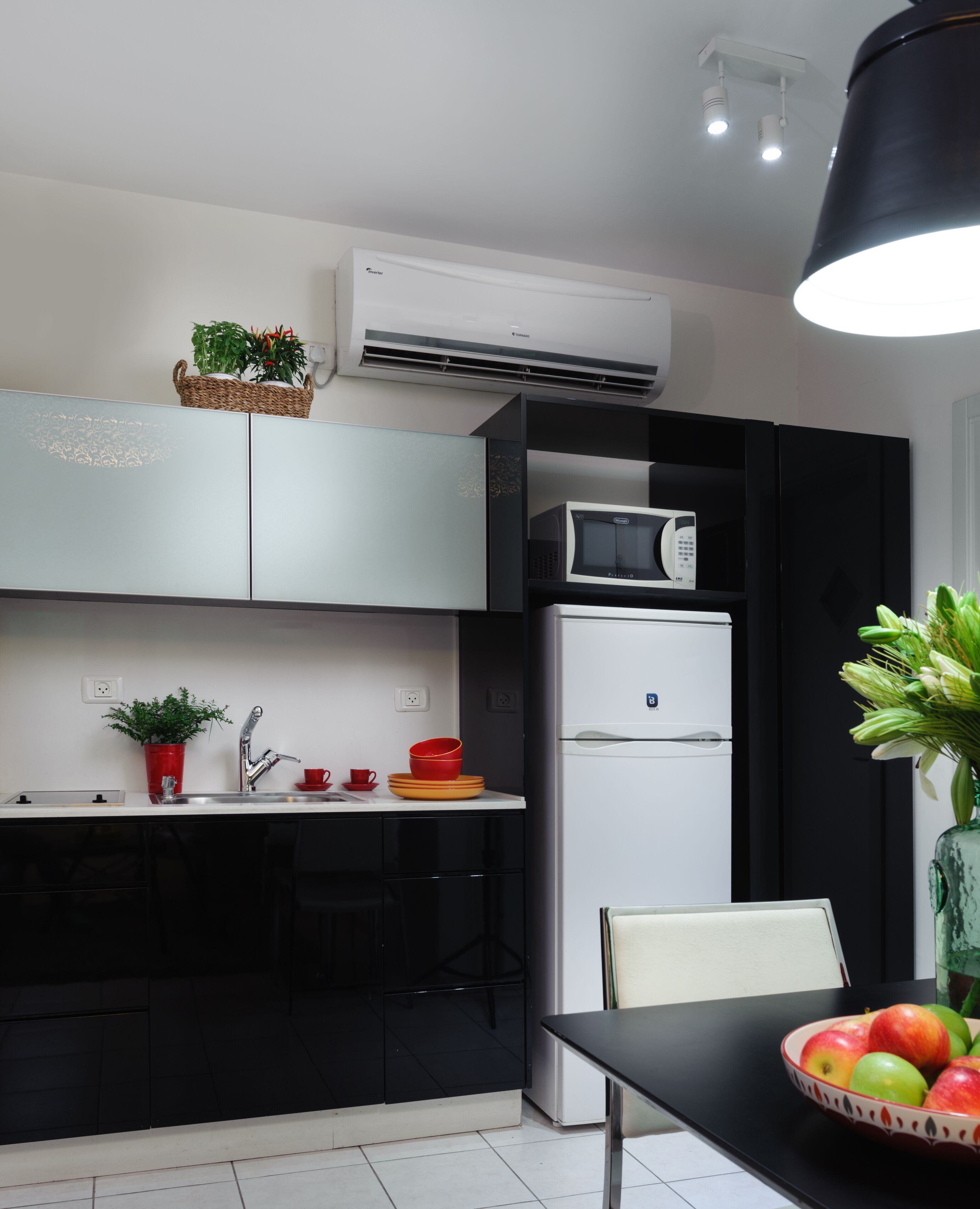 A compact kitchen with a microwave, refrigerator, and a dining table with a bowl of fruit.