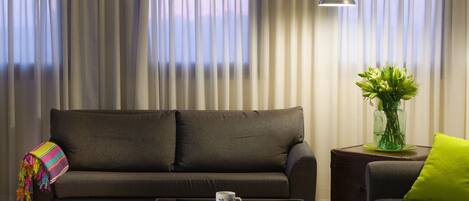 A modern living room with a sofa, a coffee table with books, a lamp, and a vase with flowers.