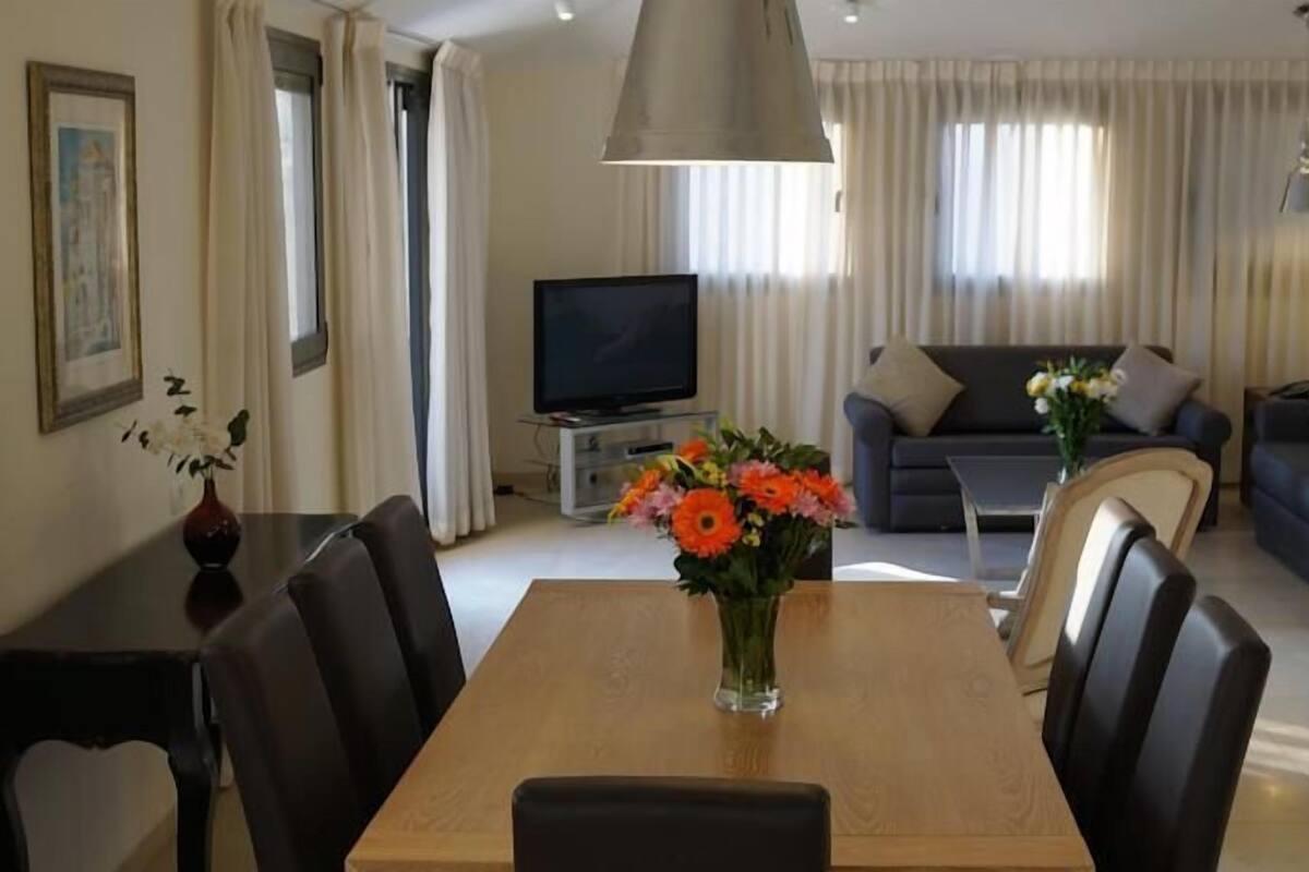 Een moderne woonkamer met een eettafel, twee banken, een televisie en een bloevas.