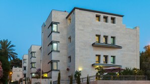 Un hôtel moderne à plusieurs étages, doté d’une façade en pierre, de balcons et d’un espace extérieur aménagé pour s’asseoir.