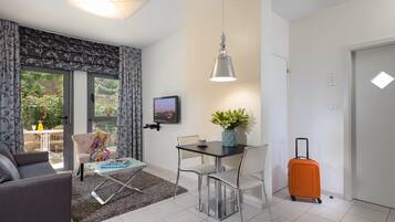 A modern living room with a sofa, a dining table with chairs, a small coffee table, a potted plant, and a suitcase.