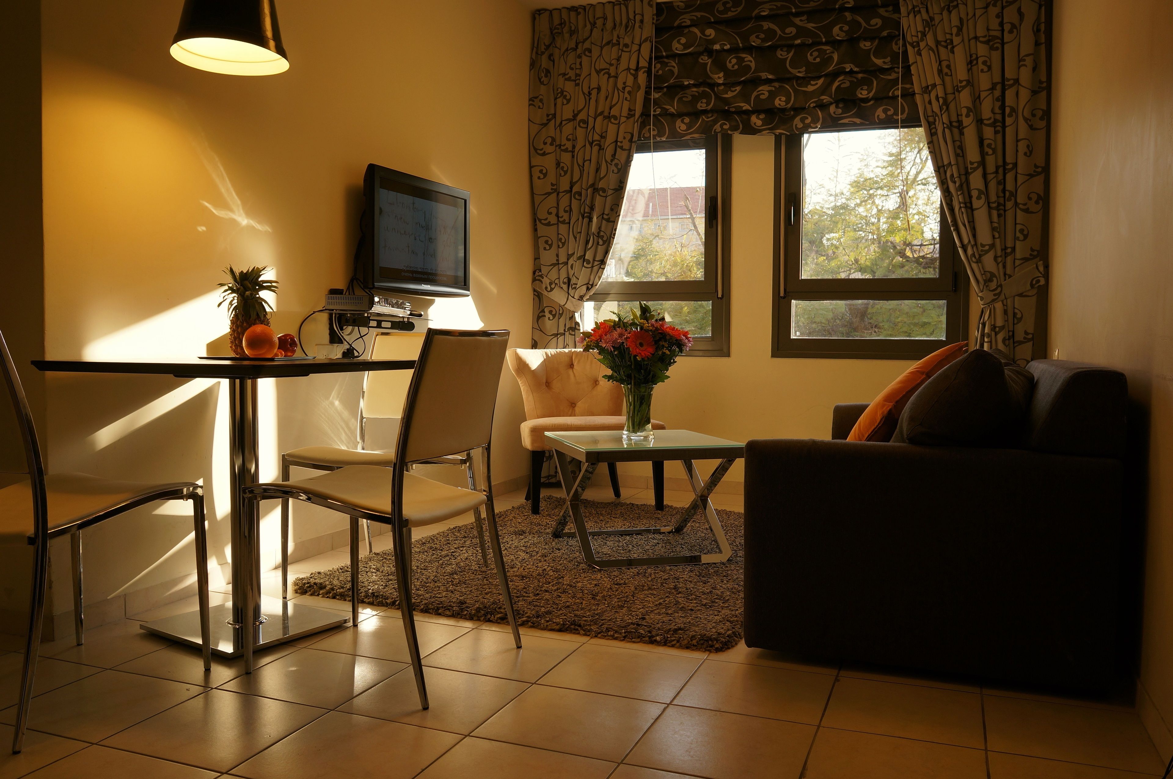 A living room with a TV, a dining table with chairs, a sofa, and a window with curtains.