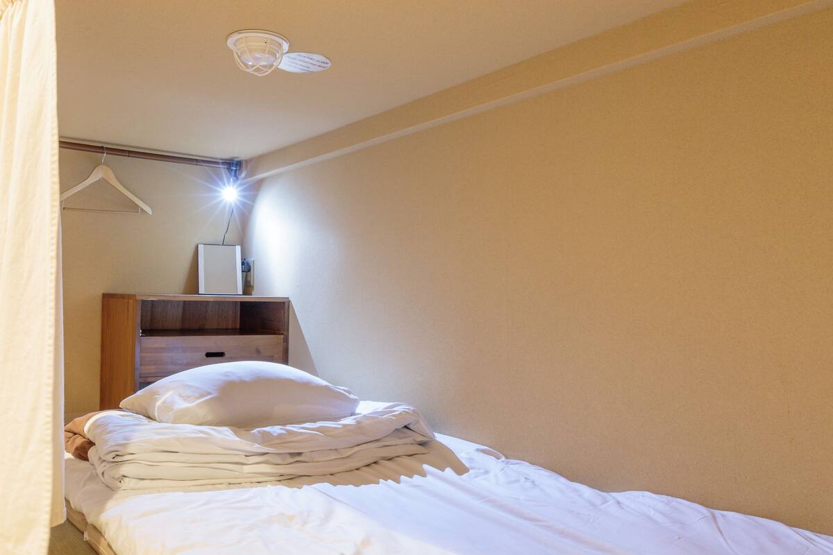 A neatly made bed in a hotel room with a wooden nightstand, a hanging light fixture, and a wall-mounted mirror.