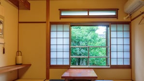 A traditional Japanese room with tatami flooring, a low wooden table, cushions, and a shoji screen window. - Gion Ryokan Q-beh - Hostel (Kyoto)