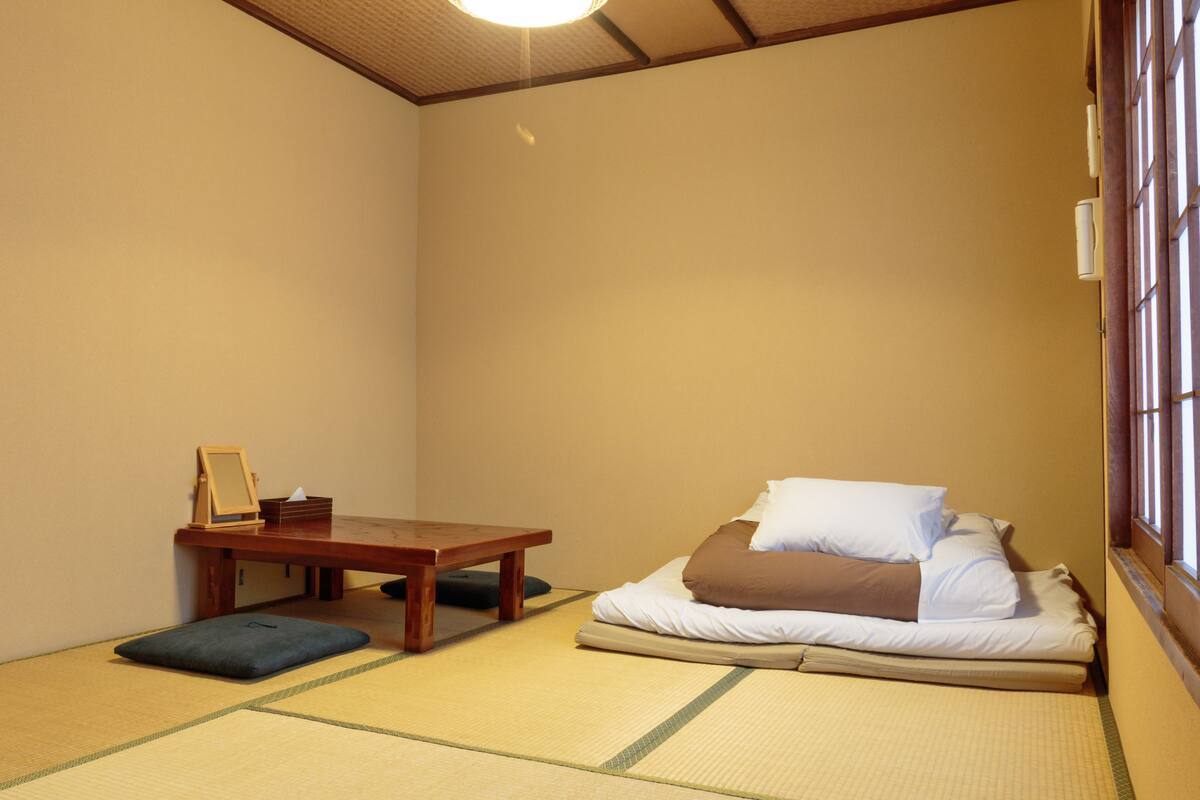 A traditional Japanese room with tatami flooring, a low wooden table, and a futon bed with pillows.