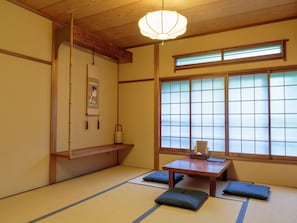 A traditional Japanese room with tatami flooring, a low wooden table, cushions, a hanging lantern, and a shoji screen window. - Gion Ryokan Q-beh - Hostel (Kyoto)