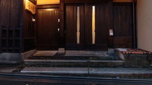 A traditional Japanese building with a wooden entrance, a tiled roof, and a stone pathway leading to the door. - Gion Ryokan Q-beh - Hostel (Kyoto)