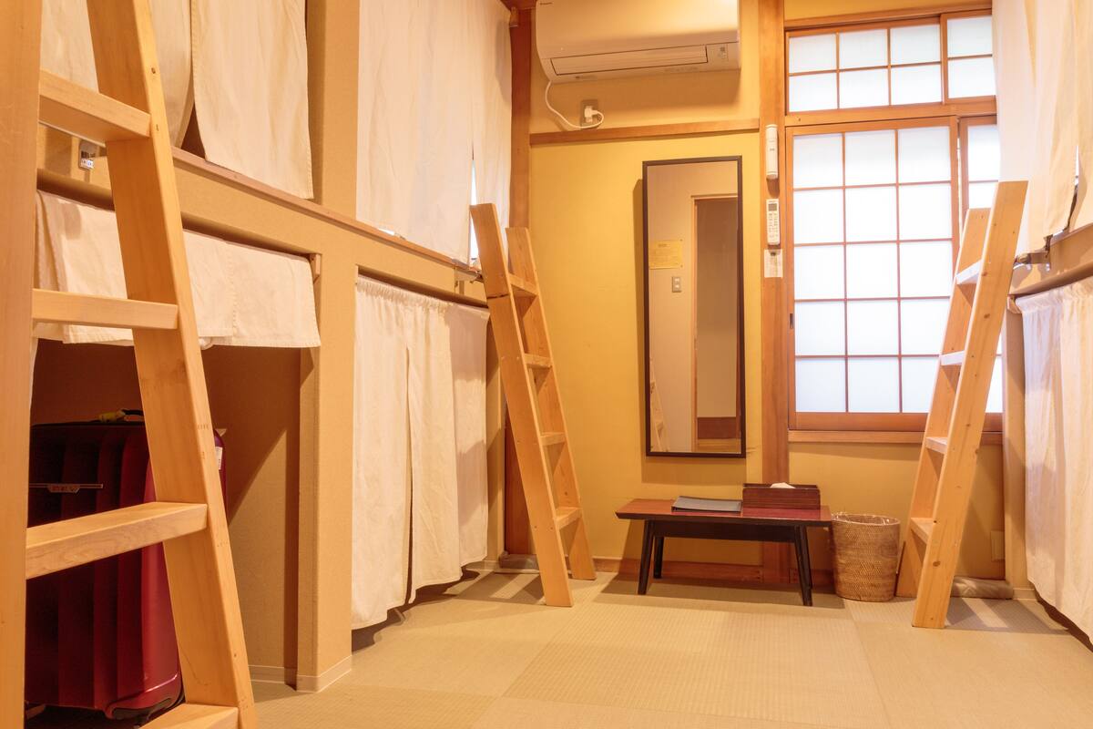 A room with bunk beds, a wooden ladder, a table, and a window with a view.