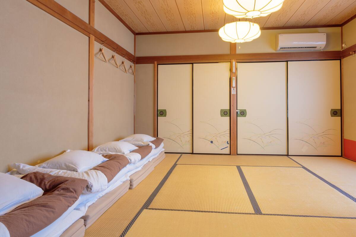 A traditional Japanese room with tatami flooring, a low bed with pillows, a sliding door with decorative patterns, and a ceiling fan.