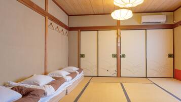 A traditional Japanese room with tatami flooring, a low bed with pillows, a sliding door with decorative patterns, and a ceiling fan.