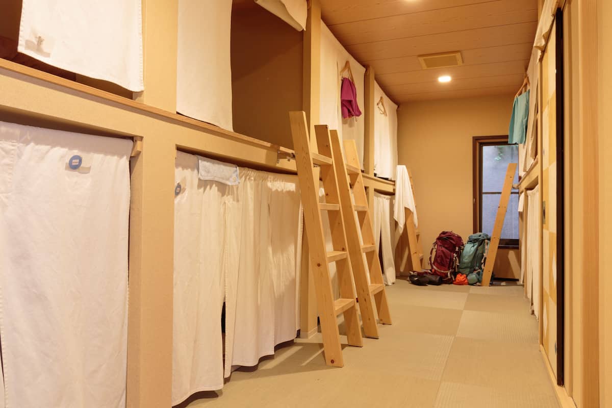 A hallway with wooden floors, a wooden ladder, and a window with curtains.